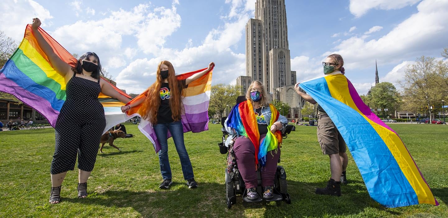 Four students holding pride flags on the lawn in front of the Cathedral of Learning