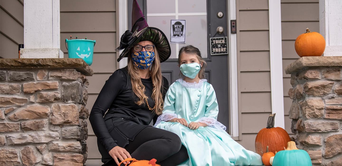 A woman and her child in costume, sitting in face masks on a porch