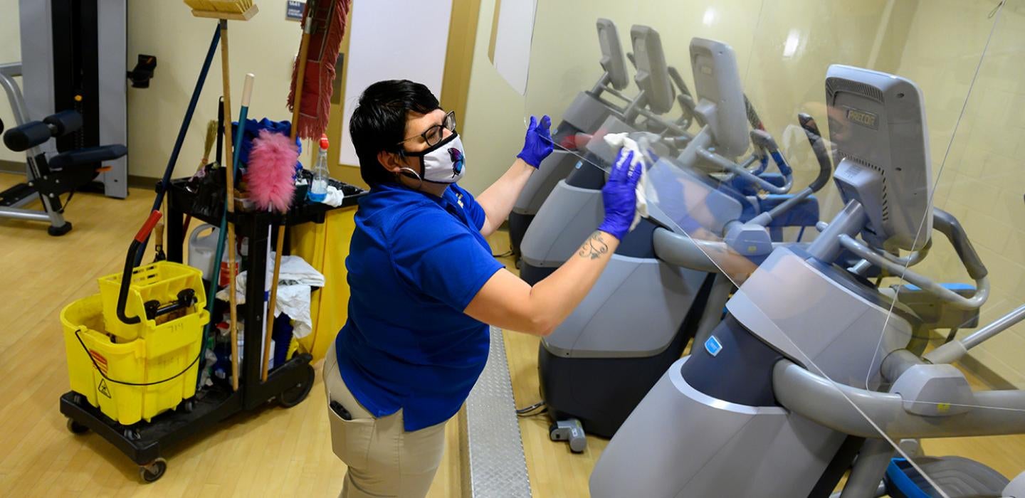 A person in blue Pitt protective gear cleans exercise equipment