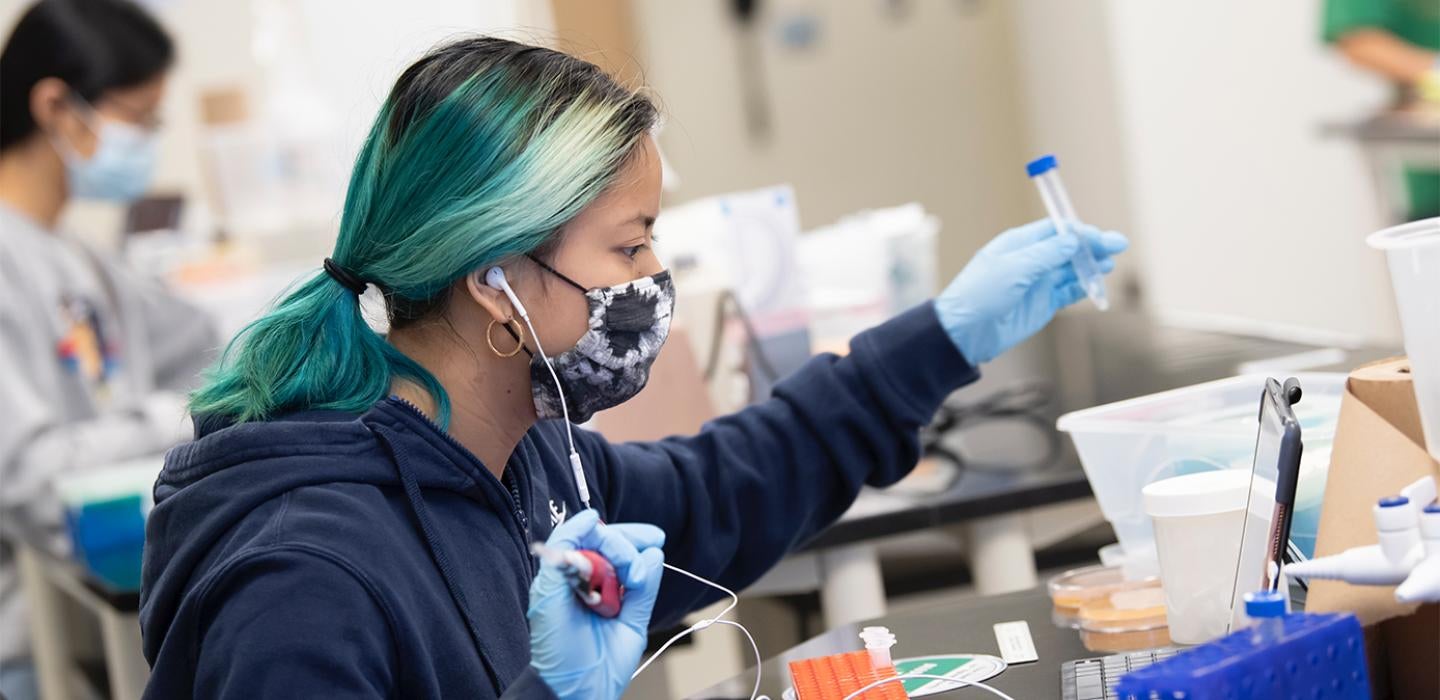 A student with blue-green and black hair uses lab equipment