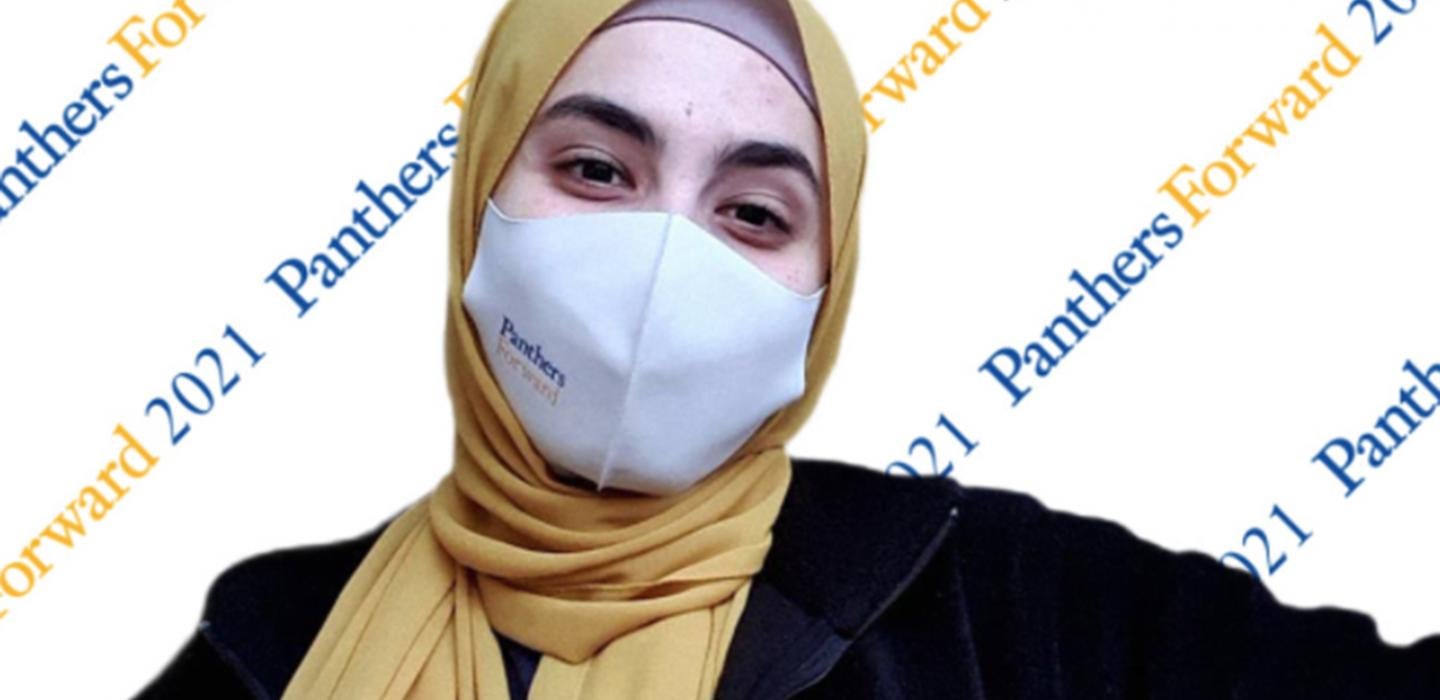 Woman in a yellow headscarf and a white mask with PanthersForward 2021 in the background