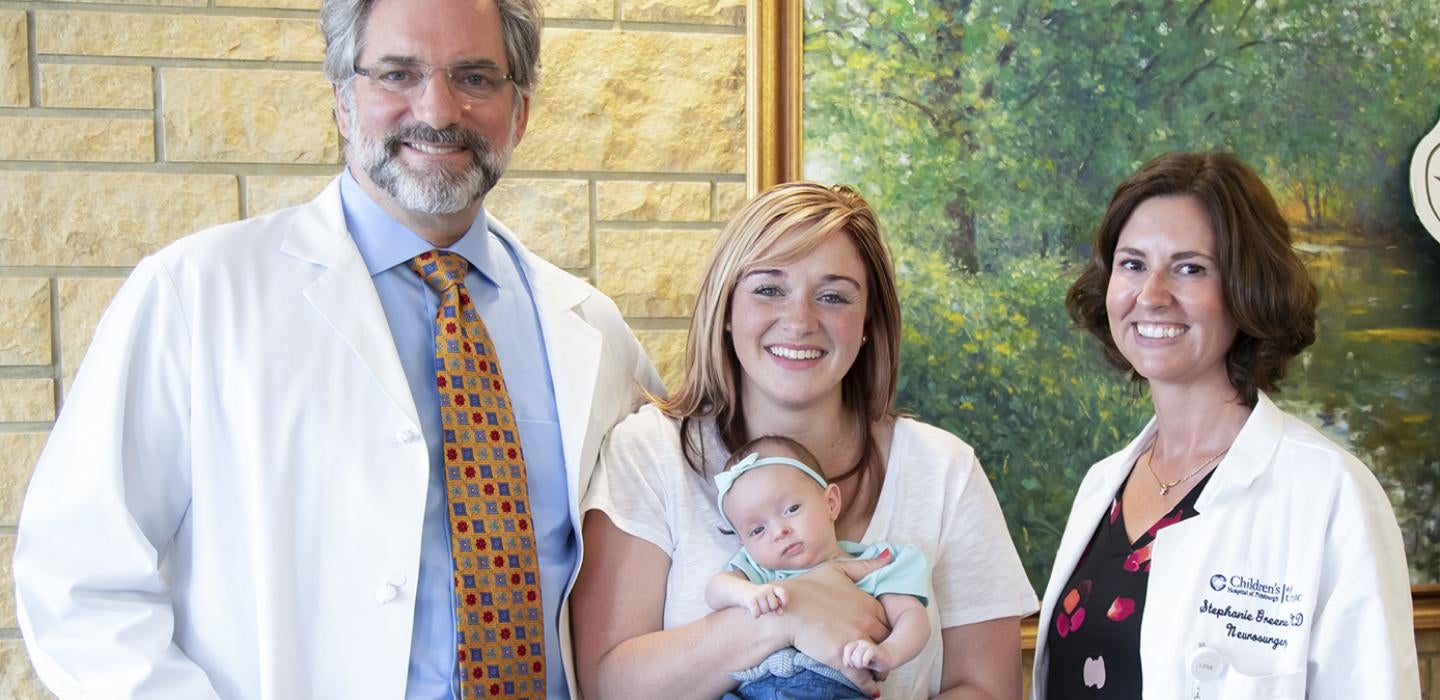 mom holding baby, flanked by the two Pitt doctors who lead the operation