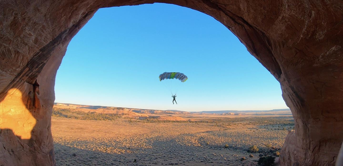 A man BASE jumping through a natural rock arch