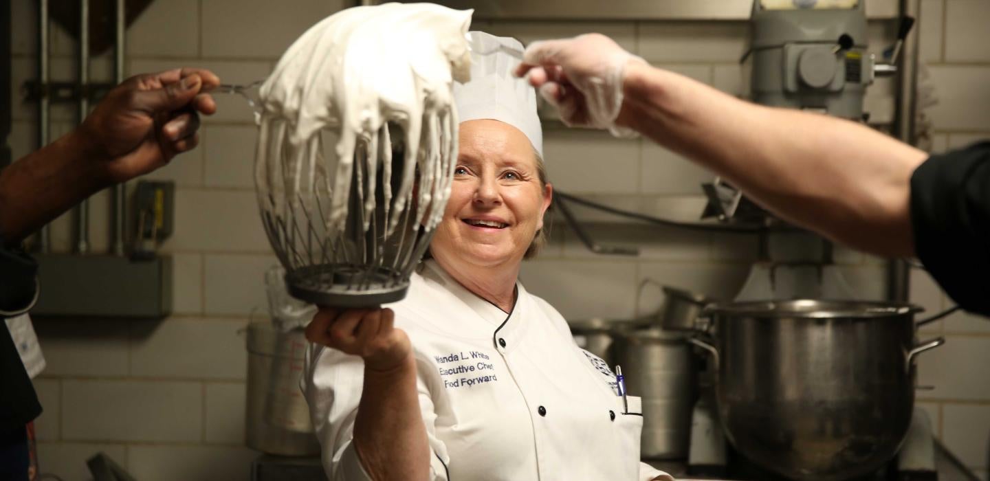 woman in a chef's hat holding up a beater covered in white cookie batter