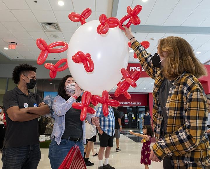 Three people sticking red balloons to a larger white balloon