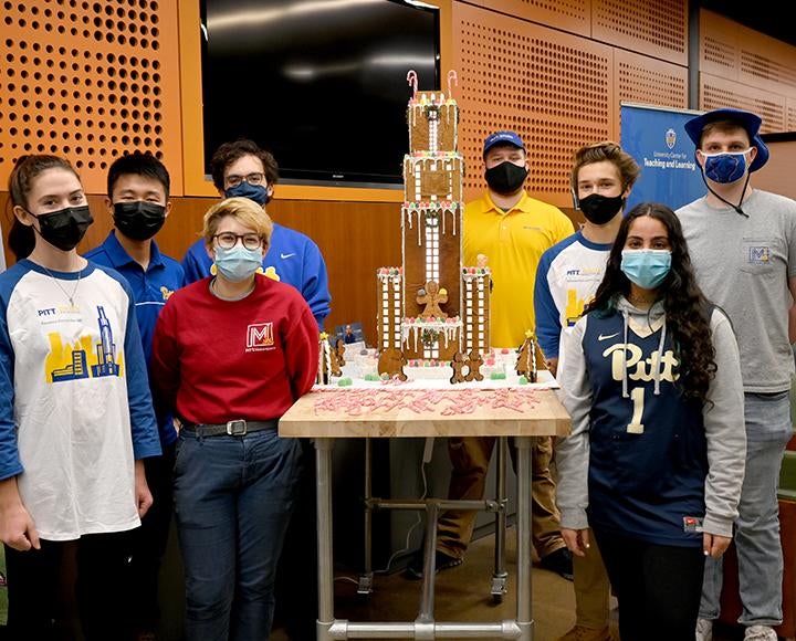 Team of students standing next to their completed gingerbread model of the Cathedral of Learning