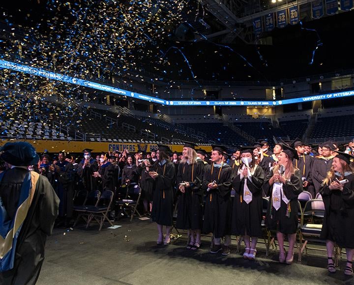 Graduating students looking up as blue and gold confetti falls from above