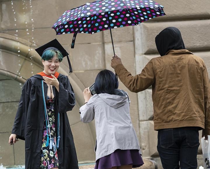 Graduating student posing for photo in the rain next to colorful umbrella