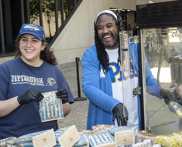 two smiling people serving popcorn