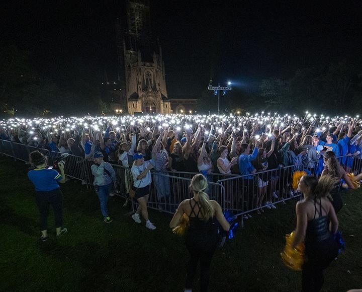 A crowd of people stand holding lights up at night.