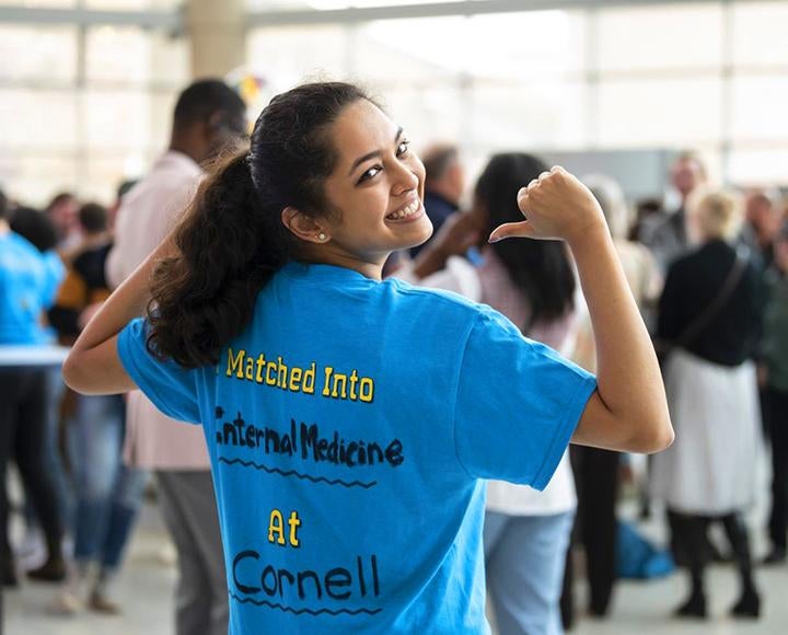 A person points at the back of their blue shirt, which reads I matched into internal medicine at Cornell