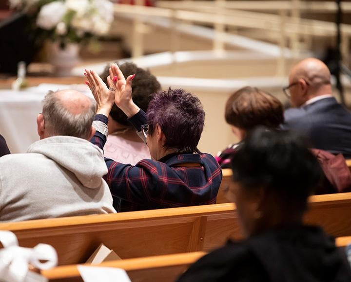 A person claps over their head while sitting among others in a church pew