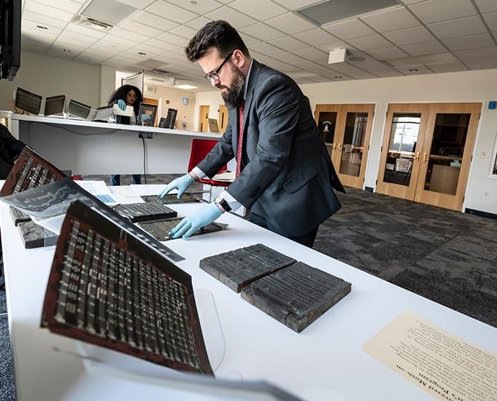 A person in a grey suit and blue gloves handles archival prints on a table