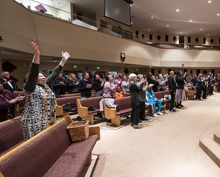 People stand and clap in church pews