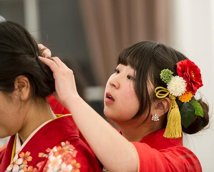 A girl in a red kimono adjusts the hair of another girl in a red kimono