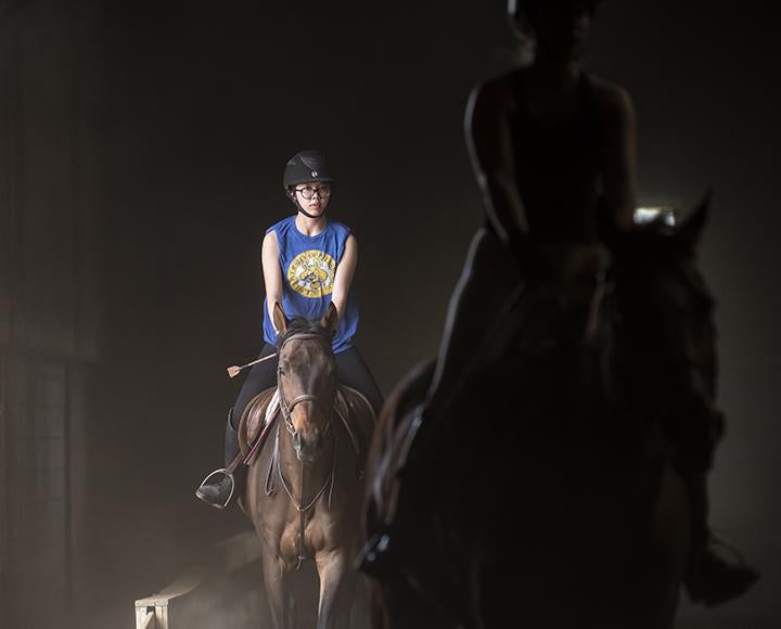 People ride on horses in a darkened arena