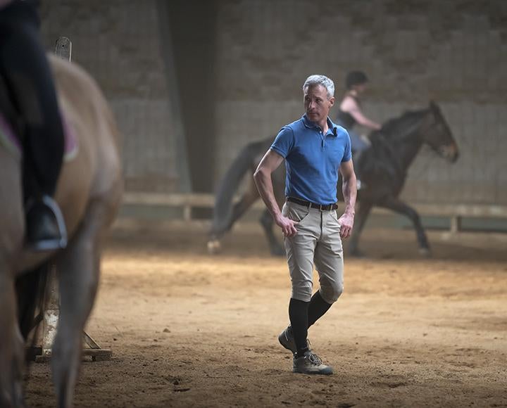 A person in a blue polo looks at people riding on horses around him