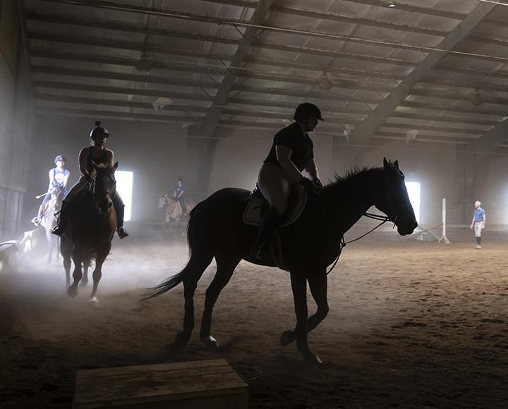 People ride on horses in a line inside a darkened arena