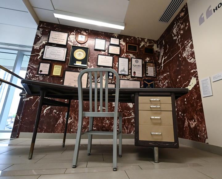 a metal desk with many framed documents hanging on the wall behind it