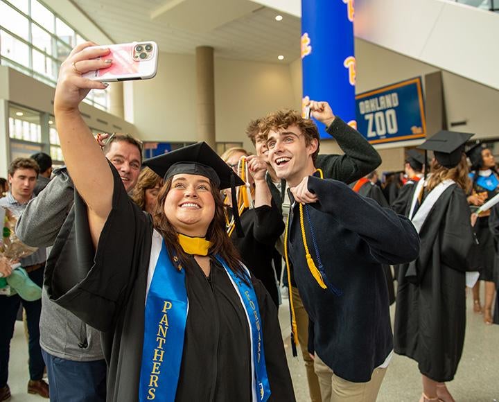 A person in graduation regalia takes a selfie with friends