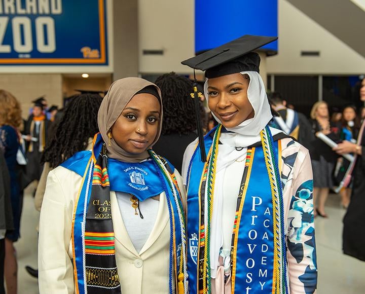 Two people in multicolored stoles and cords and black graduation caps