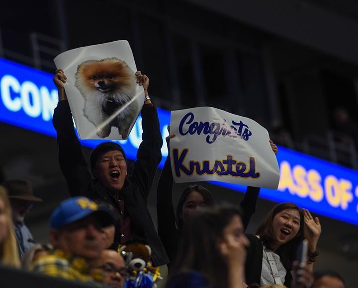 People hold up a poster of a shiba inu and a poster that reads Congrats Kristel