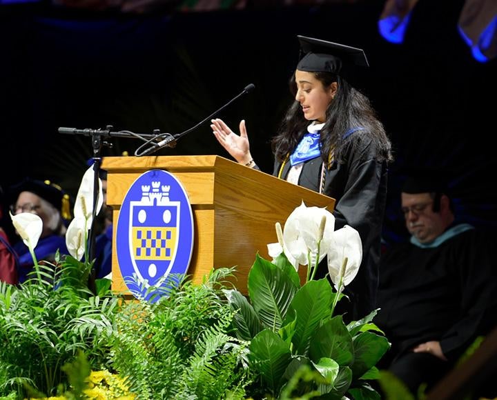 A person in graduation regalia speaks at a podium