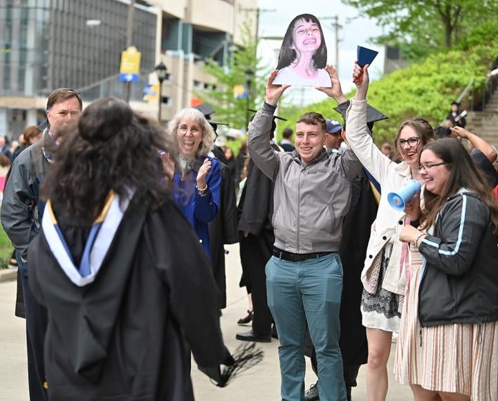 A person holds up a photo cutout of a smiling child while others clap and hold up noisemakers