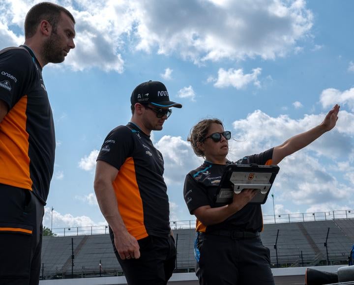 Three crew members look at an iPad as they watch the racetrack