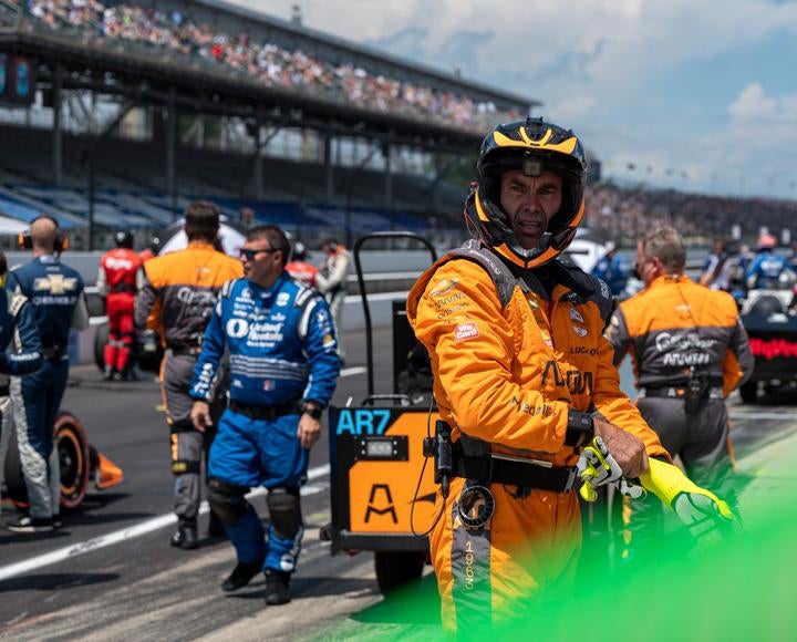 A driver in an orange jumpsuit and helmet