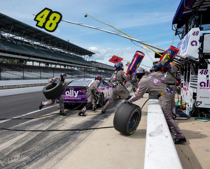 A pit crew changes tires on a purple racecar