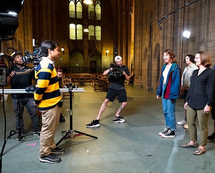 A videographer leans with a camera to film a tour group in the Cathedral of Learning
