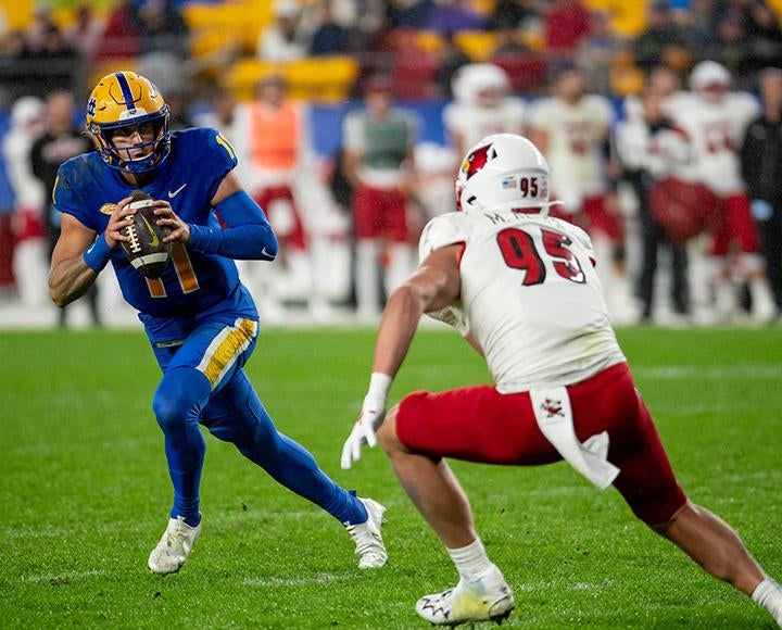 A quarterback in Pitt gear runs by a Louisville defenseman