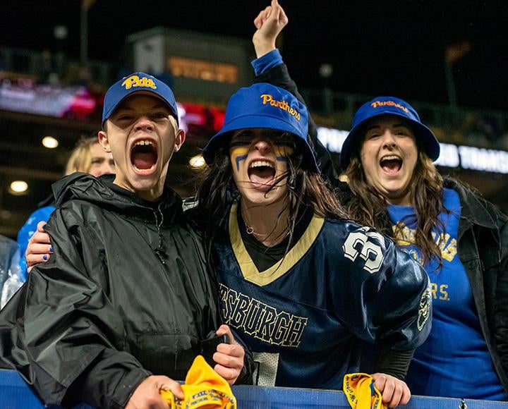 Fans in Pitt gear scream at the camera from the stands