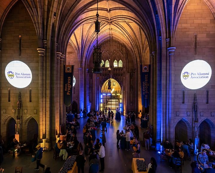 Two Pitt Alumni Association logos are projected onto the walls of the Cathedral of Learning grand hall