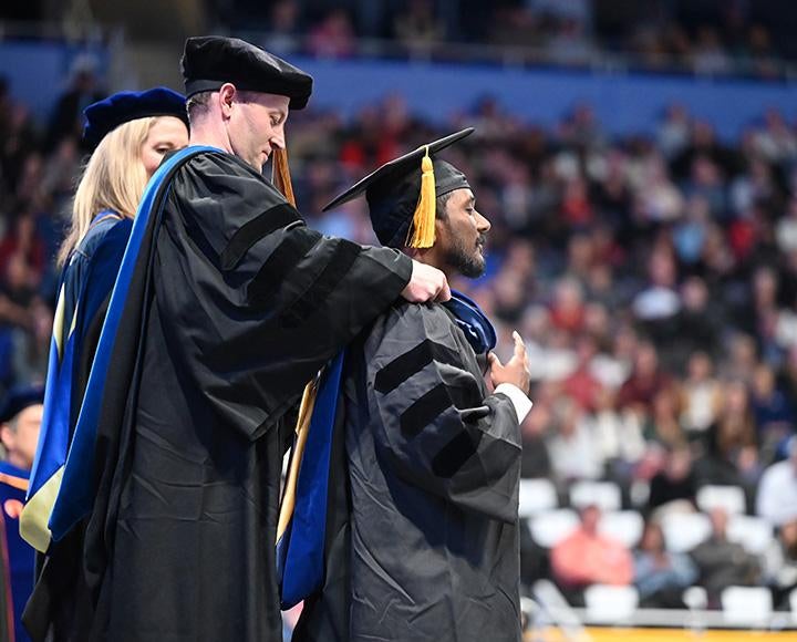 A person places a hood over a graduate student
