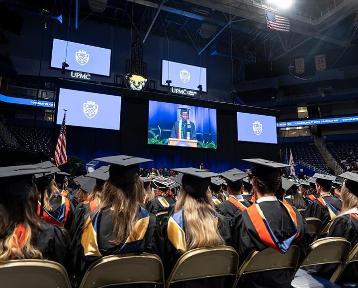 A person on a screen delivers an address to graduates