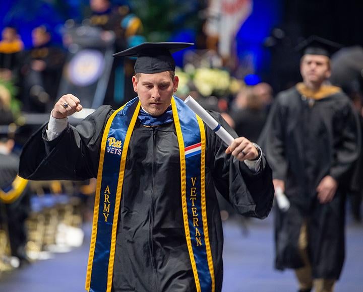 A person in graduation robes and an Army Veteran stole fist pumps with his diploma