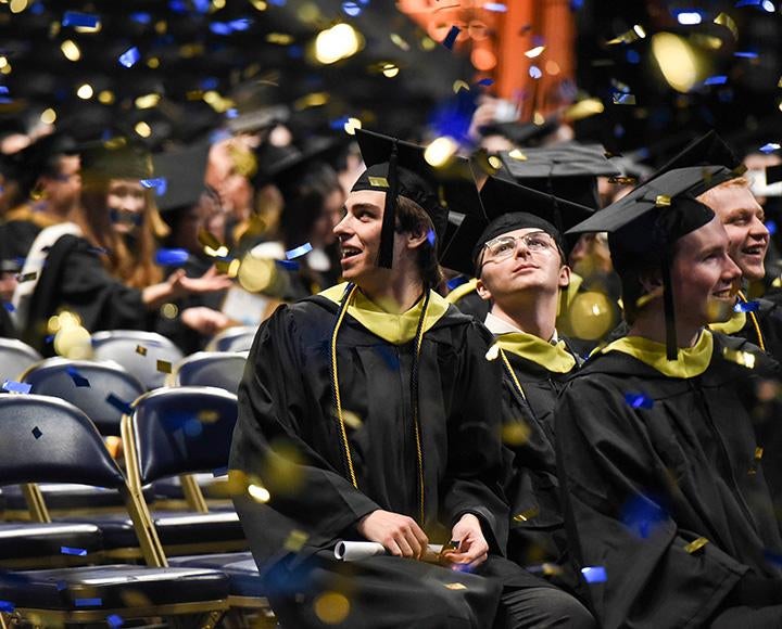 Graduates smile up at falling confetti
