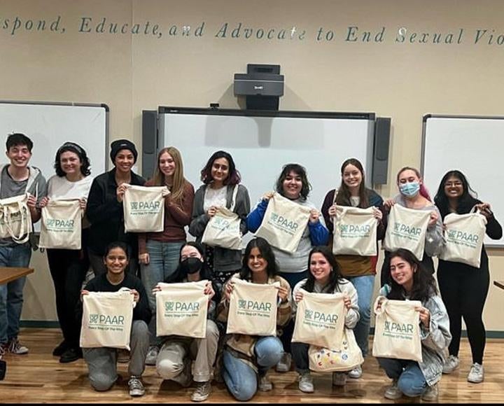 A group of peer educators hold up tote bags