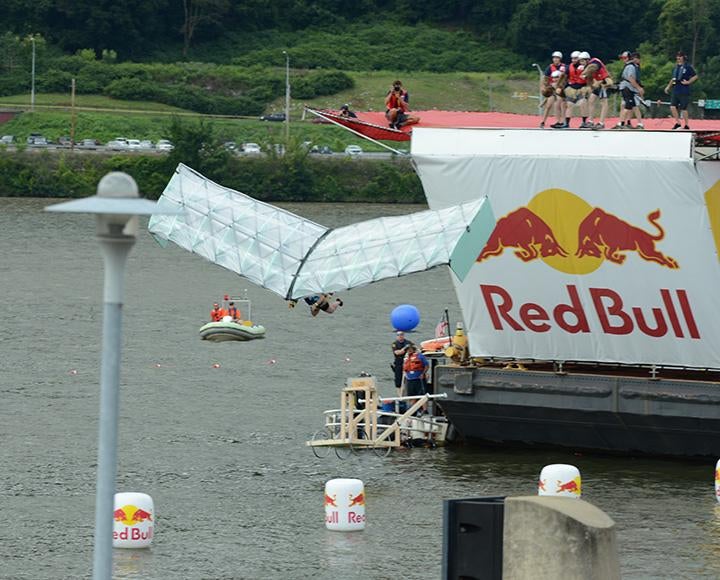 A person with a glider falls into the water from a platform with the Red Bull logo
