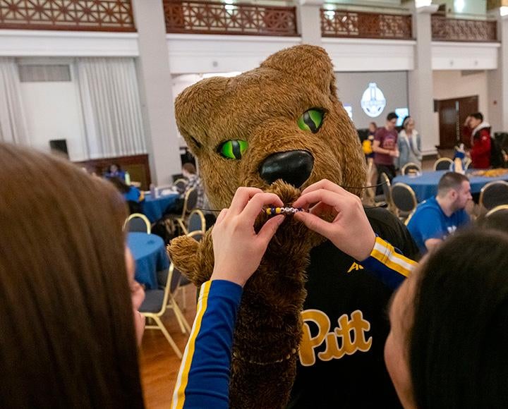 A person puts a beaded friendship bracelet on a panther mascot