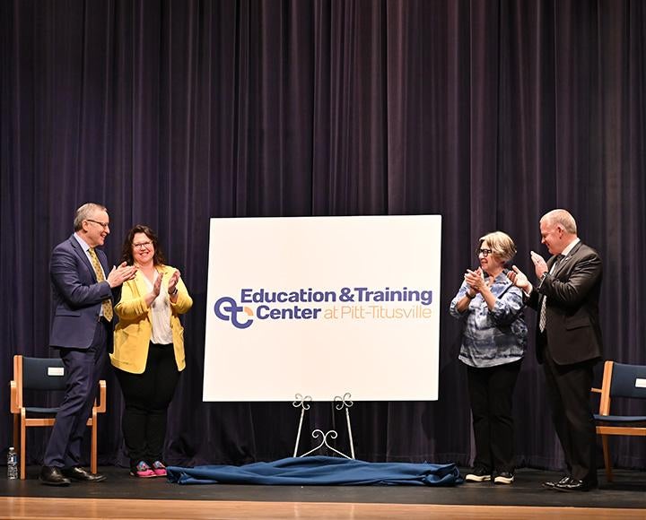 Four people clap around a poster for the Education and Training Center at Pitt-Titusville