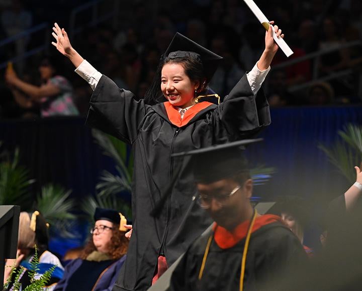 A graduate spreads their arms as they exit the stage