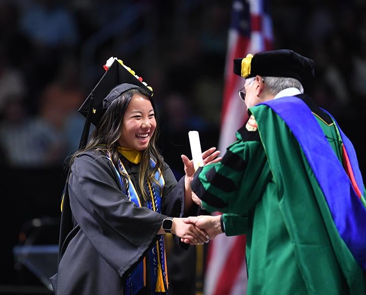 A graduate receives her diploma from a faculty member