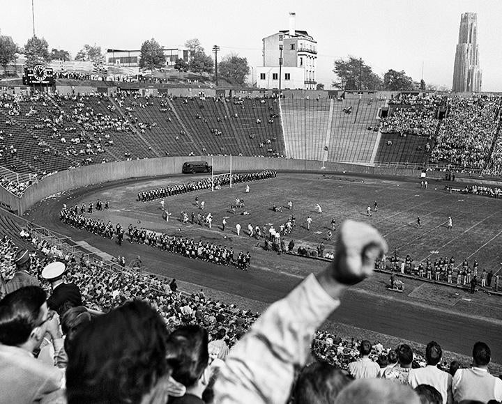 A black and white photo of people cheering for the marching band at Pitt Stadium