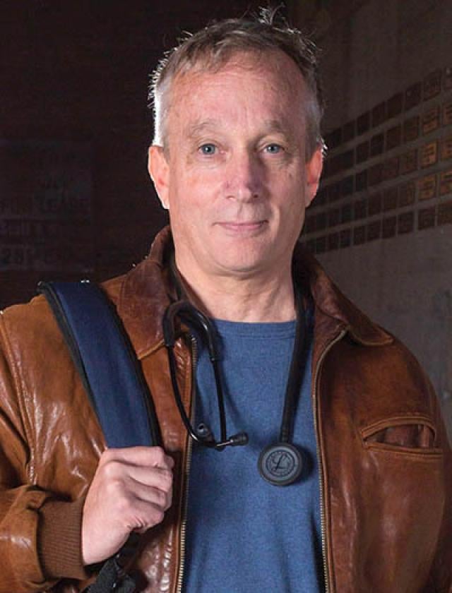 Jim Withers in a leather jacket holding a bag