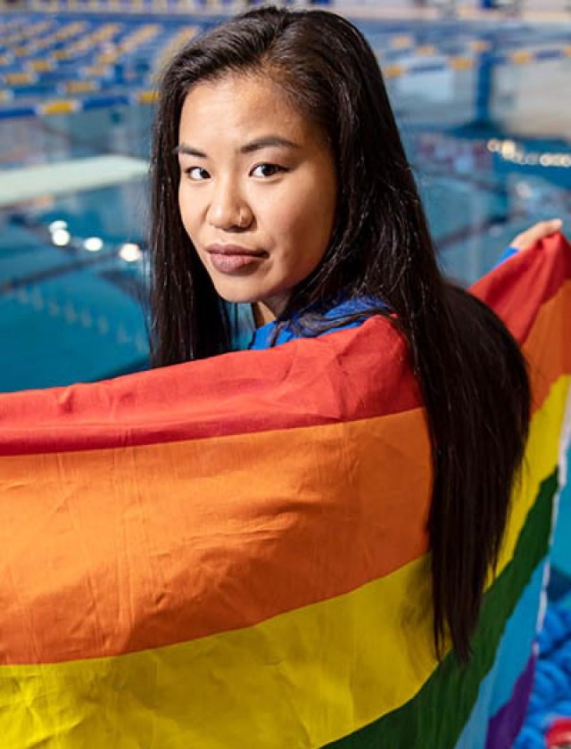 Lisa Coe in front of a pool, holding a rainbow flag