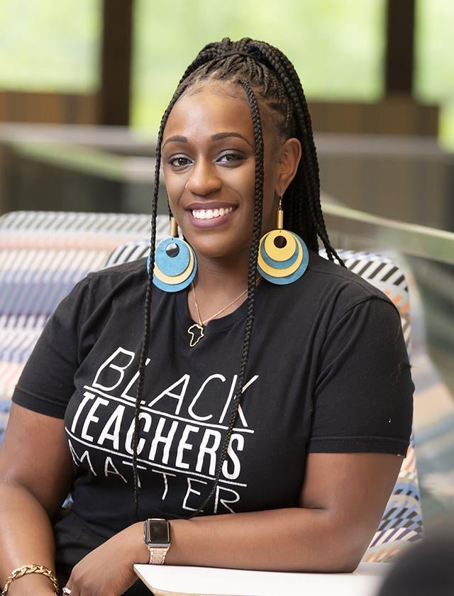 Brianna Ross sits wearing a black shirt that reads Black teachers matter