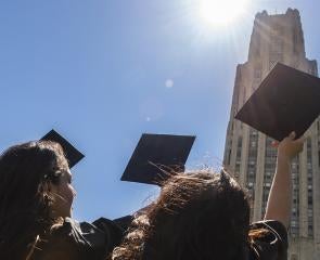 Pitt graduates pointing caps towards the Cathedral of Learning 